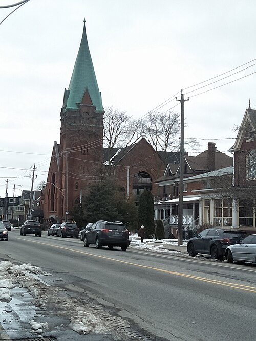 A former Presbyterian church on Annette Street with a copper spire and a red brick bell tower, now condominiums called Victoria Lofts, houses on either side.