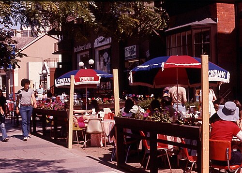 An outdoor cafe on Yorkville Avenue in July 1978, red and white umbrellas over the tables and pedestrians on the sidewalk.