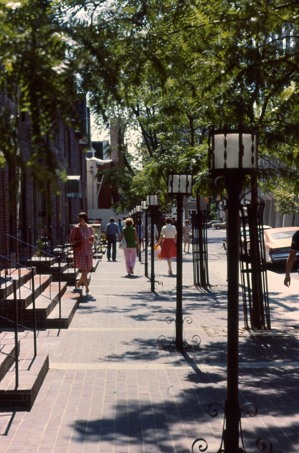 Yorkville Avenue in 1974, pedestrians on a brick sidewalk lined with wrought iron lampposts and rowhouses converted into shops.