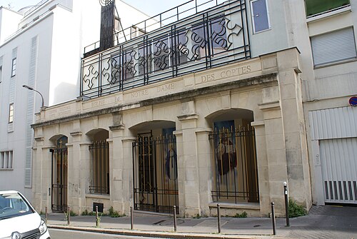 The front of Notre-Dame-des-Coptes on rue de l'Est, five stone arches closed by iron gates, with the church's name cut into the entablature and a rail of Coptic crosses along the balcony above.