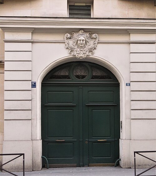 A dressed stone carriage entrance at 6 and 6 bis rue Saint-Fargeau, dark green doors under a round arch with a carved woman's head above the keystone.