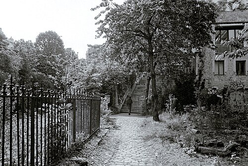 A cobbled lane with iron railings along one side and a brick building along the other, running to a flight of stone steps with one person coming down them.