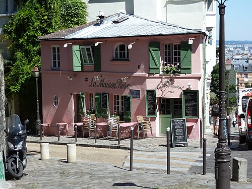 La Maison Rose at the corner of rue de l'Abreuvoir, pink walls and green shutters, with folding tables out on the cobbles and chalkboard menus either side of the door.
