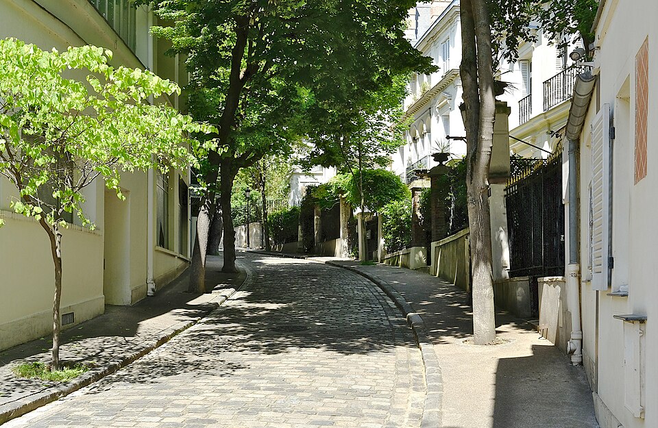 Inside avenue Frochot, a cobbled lane curving away between garden walls, with plane trees on both sides and white houses with shutters and iron balconies behind them.