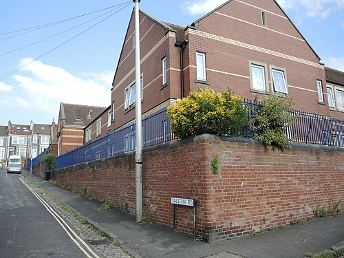 Red brick terraced houses built into the former Bristol School Board buildings at the corner of Beauley Road and Dalston Road, behind a high retaining wall.