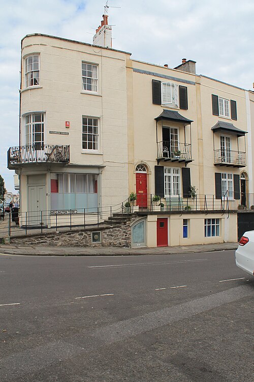 A curved corner terrace in cream stucco, wrought iron balconies over bow windows, and a red front door at street level.
