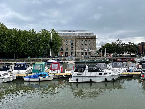 The Arnolfini's stone warehouse front behind a marina crowded with small pleasure boats moored side by side.