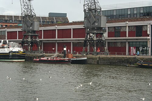 The steam tug Mayflower and the fireboat Pyronaut moored under cranes 29 and 30, the M Shed's red shed doors behind them.