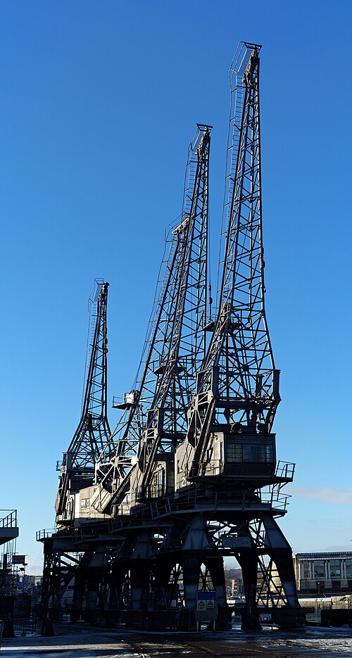 Three of Princes Wharf's electric cranes seen from the quay, their lattice jibs cutting a silhouette against open sky.