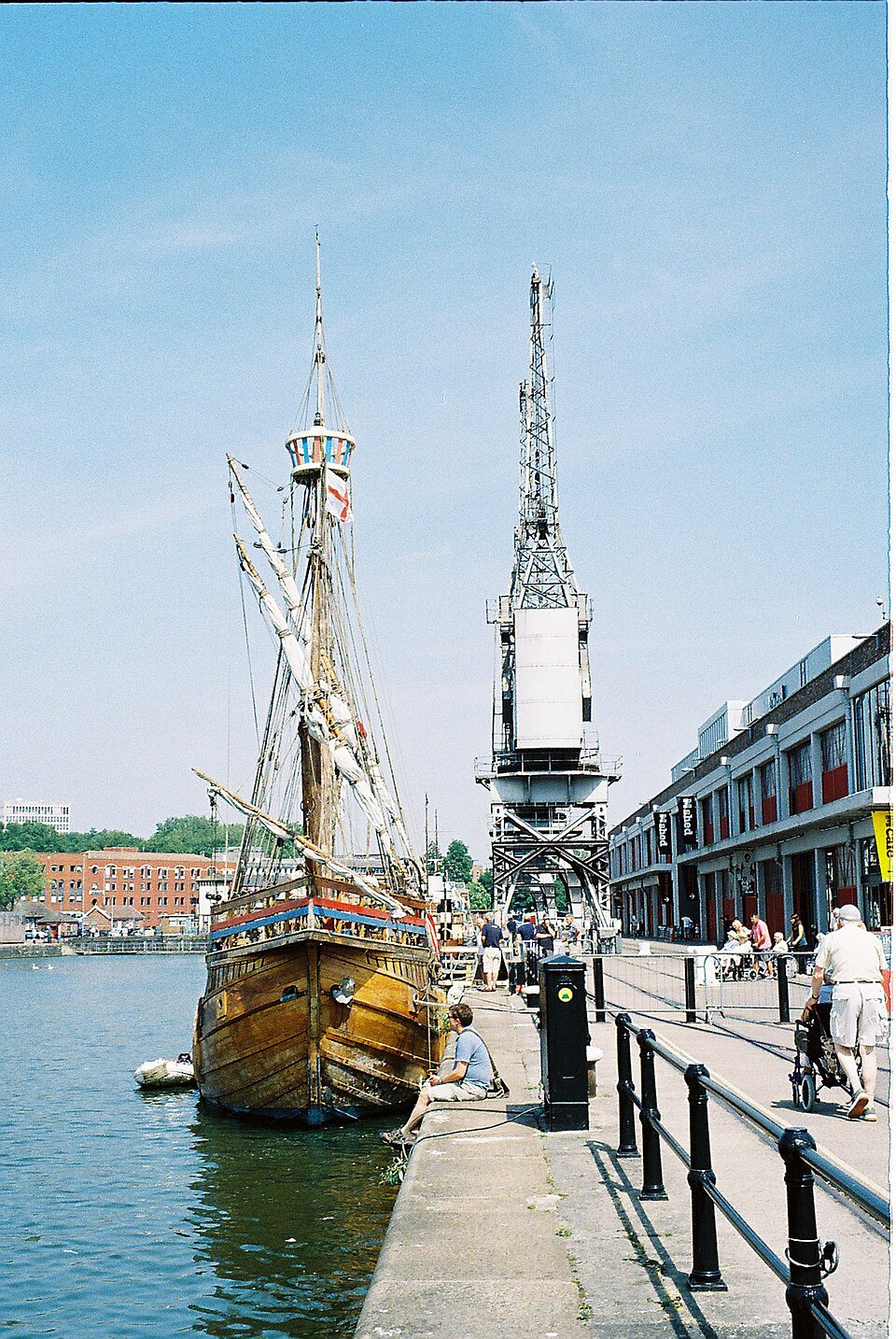 The wooden replica ship the Matthew moored bow on beside a crane, its single mast and rigging against the sky, M Shed behind.