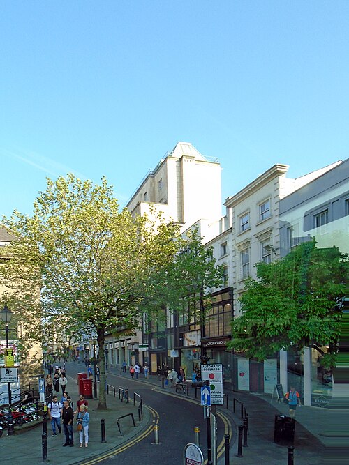 The bottom of Bold Street from the Hanover Street end, plane trees along the left pavement and a red pillar box at the kerb.