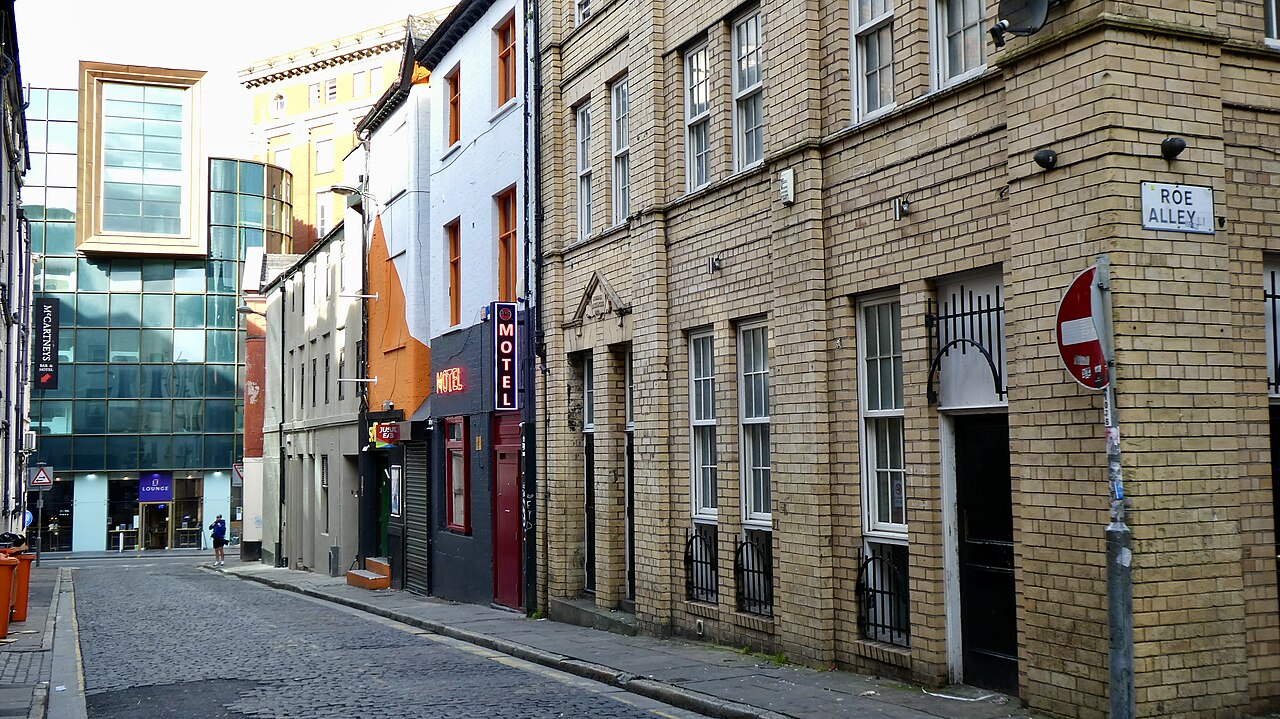 Fleet Street on stone setts, buff brick buildings along the right with a Roe Alley sign at the corner and a neon MOTEL sign further down.