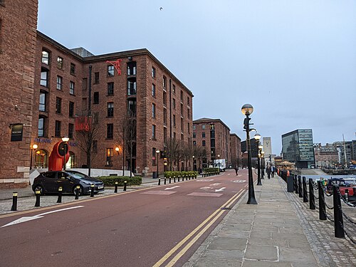 The Atlantic Pavilion warehouse from the roadway, arched openings along the ground floor, a red street sculpture on the pavement, granite kerb and road markings in front.