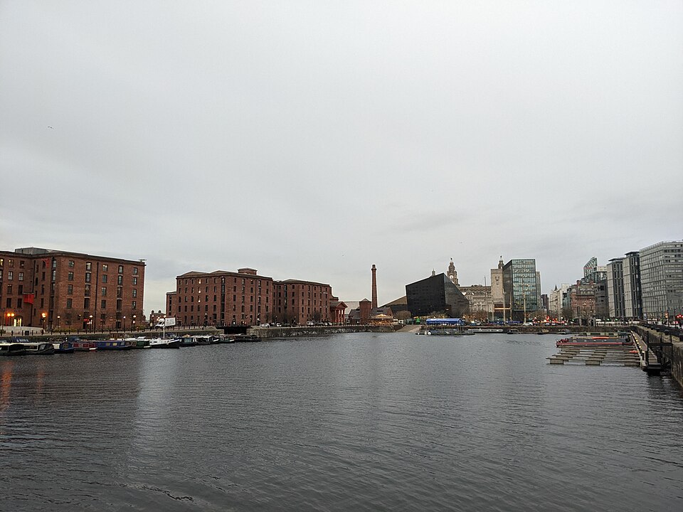 The dock basin looking toward the Pier Head, the pump house and its chimney at the water's edge, a warehouse block along the left side and the Liver Building visible in the distance.