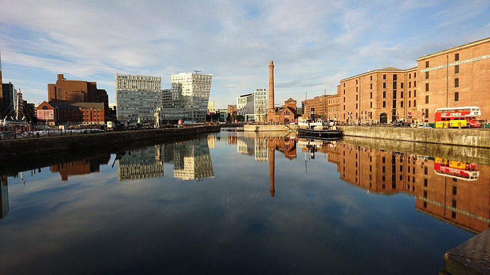 The Merseyside Maritime Museum's warehouse block across the dock basin, its name lettered in white along the top floor, the pump house and chimney reflected in the water in front of it.