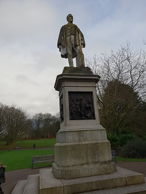 The bronze statue of William Rathbone on a tall granite plinth in the open meadow, a path and benches at its foot.