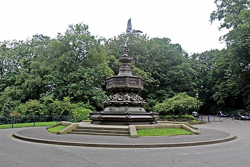 The Shaftesbury Memorial fountain, a bronze winged figure over an octagonal stone base, on a paved circle ringed by trees.