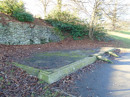 A sandstone retaining wall and the stone base of a demolished shelter beside a park path, leaves banked against it.