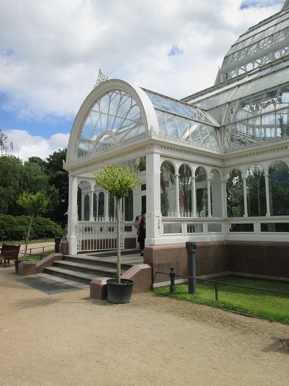 The Palm House's white painted glass entrance porch and arched dome from ground level, stone steps and a paved forecourt in front of it.