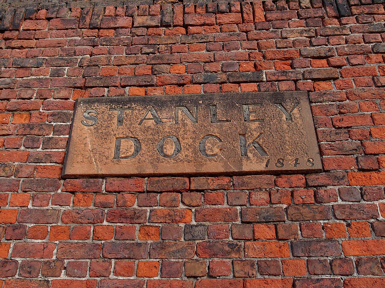 A carved stone plaque reading STANLEY DOCK 1848, set into the dock's red brick perimeter wall.