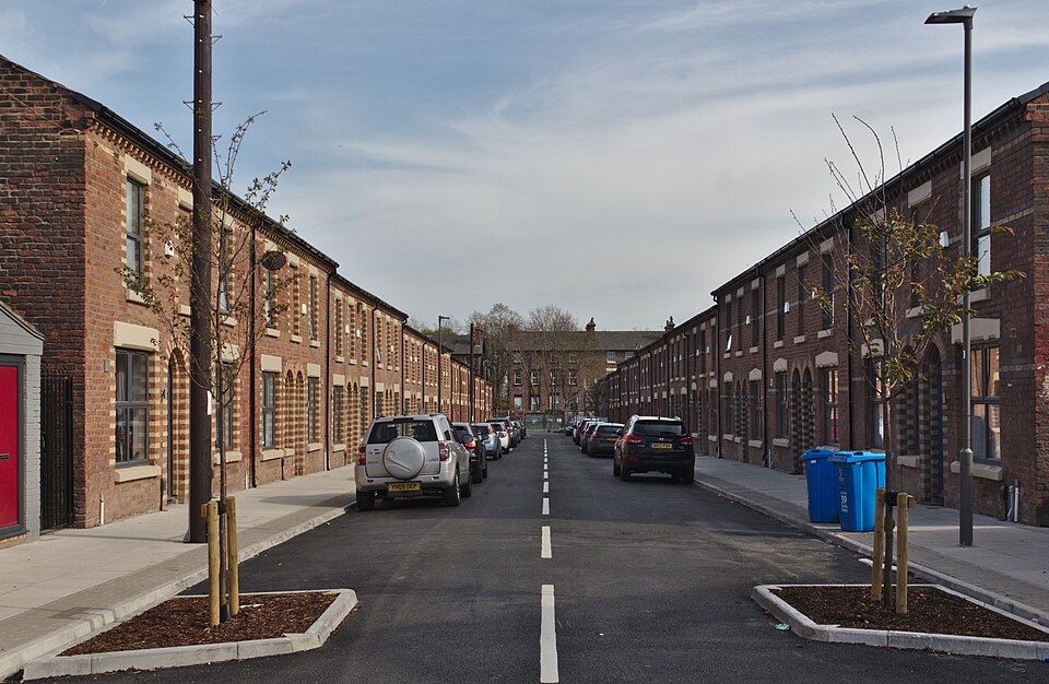 Refurbished two storey brick terraces facing each other across a newly paved street, stone window surrounds and young street trees.