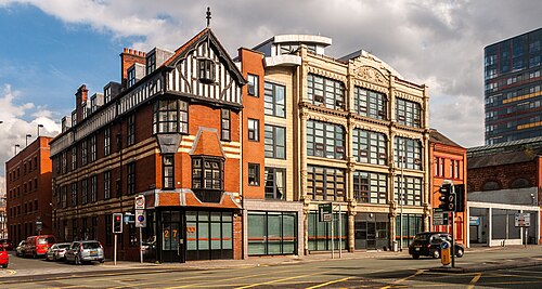The Derros Building on George Leigh Street, a black and white timbered gable and bay window over red brick banding on the corner, a stone fronted office block next to it.