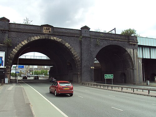 Two dark brick viaduct arches span the ring road at Dawson Street, a carved stone date plaque set into the pier between them.
