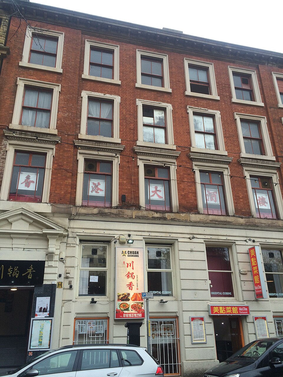 A four storey brown brick former warehouse on Faulkner Street, arched window heads in stacked rows above ground floor restaurant fronts. Neither source names the exact building used for the police station scenes, which is the Street View beside it.