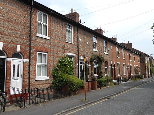 A terrace on Old Oak Street, plain red brick fronts with round headed doorways and white sash windows, small fenced front gardens along the pavement.