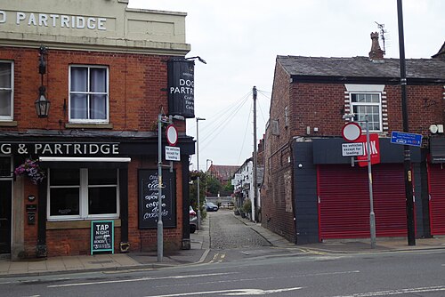 A red brick corner pub at the top of the cobbled lane, its name board over the door and hanging baskets on either side.