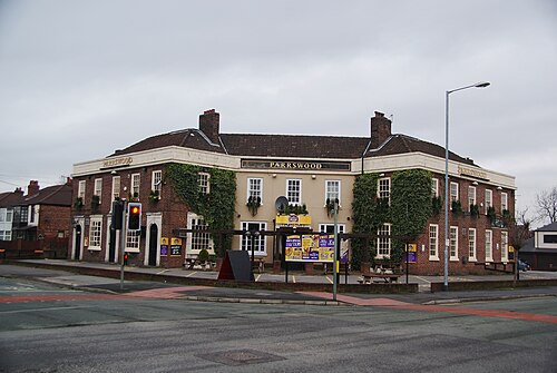 An ivy covered red brick and render pub on two storeys, chimney stacks at both ends and picnic tables out front.