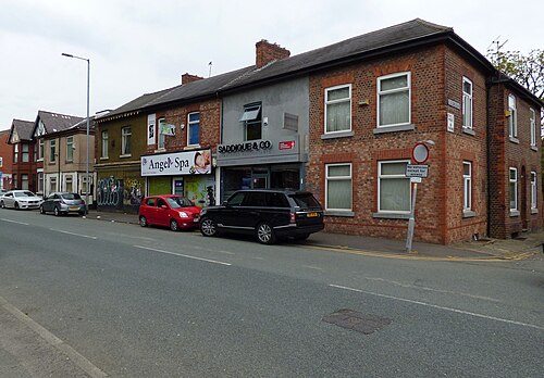 A terrace of shops on Dickenson Road, Angel Spa and Saddique and Co Chartered Accountants under flat fronted upper floors, cars parked along the kerb.