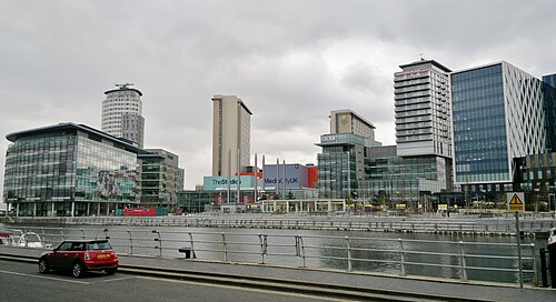 The dock basin at MediaCityUK, glass office and studio blocks lining the far quay with BBC signage visible on one.