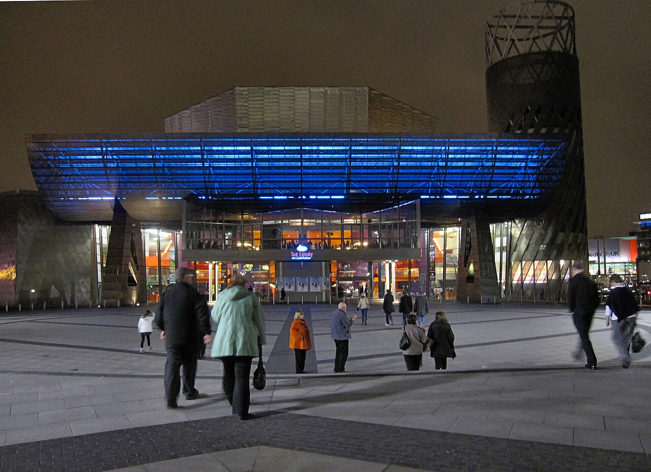 The Lowry lit up after dark, its stainless steel form catching light across the paved entrance plaza.