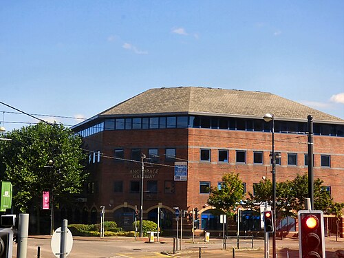 Anchorage Gateway, a brown brick office block from the early redevelopment, ribbon windows facing a road junction with tram wires overhead.