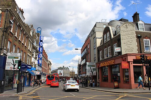 Camden High Street on the approach to the Britannia junction, an Odeon sign on the left, buses in the road and a corner pub carrying Truman Hanbury Buxton lettering on the right.