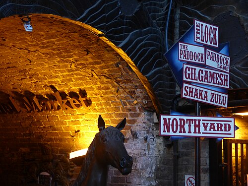 A brick barrel vault in the Horse Tunnel Market under orange light, with a bronze horse in the foreground and fingerposts to the market yards.