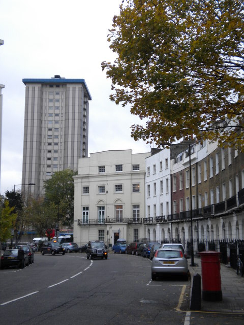 Mornington Place looking east towards the curved stucco terrace of Mornington Crescent, a white corner house in the middle of the frame and a tower block behind it.