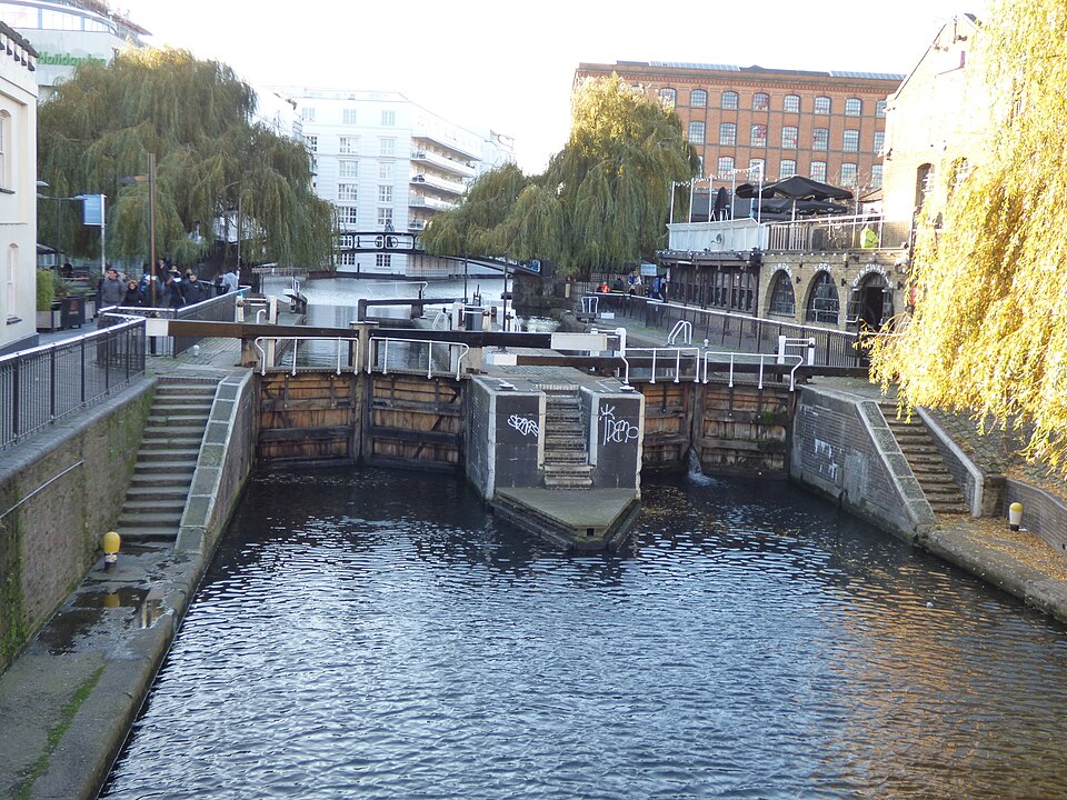 The twin chambers of Hampstead Road Lock from the road bridge, gates shut, willows on both banks and the market buildings behind.