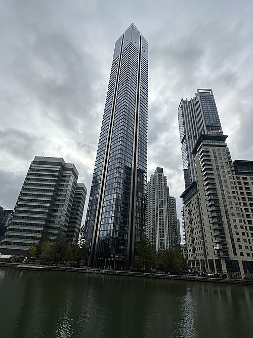 South Quay Plaza from across the dock, a tall glass residential tower with balconies, an older office block on the left and more flats on the right.