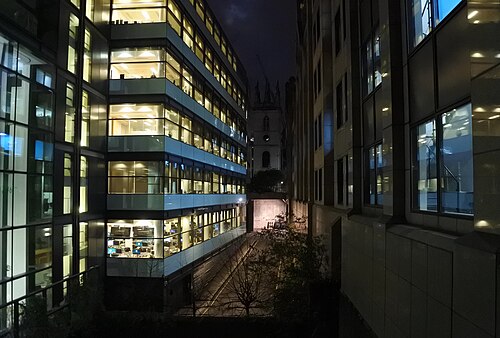 Castle Baynard Street at night, a lower level of roadway between lit office floors, with the tower of St Mary Somerset at the far end.