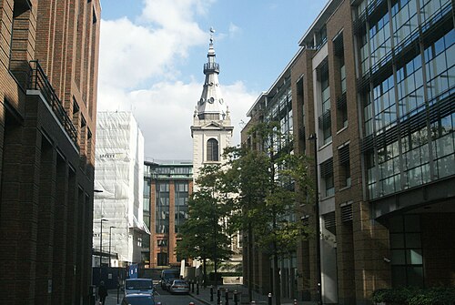 The steeple of St Nicholas Cole Abbey at the end of a narrow street off Peter's Hill, modern offices along both sides and young trees on the pavement.