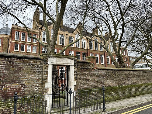 The old Hugh Myddelton School behind the brick wall around its yard, with a stone gateway in the wall carved GIRLS INFANTS and plane trees on the pavement.