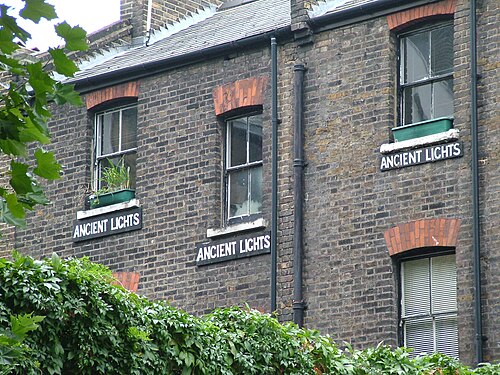 Three ANCIENT LIGHTS signs fixed under the windows of a brick building, seen from St John's Square.