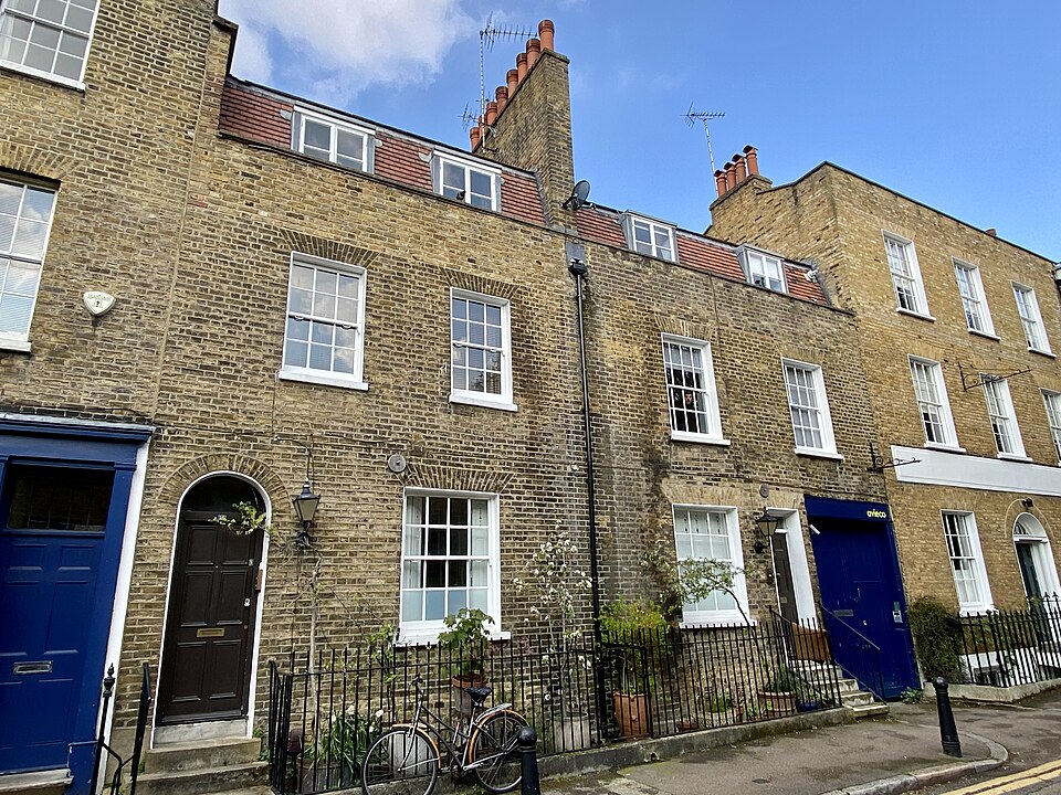 Houses on St James's Walk in yellow stock brick, sash windows and dormers above, a round arched doorway with a dark timber door and black railings along the pavement.