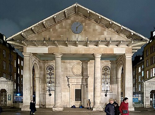 The east portico of St Paul's Church floodlit at night, four Tuscan columns under deep eaves, a clock in the pediment and a plaque where the middle door would be.