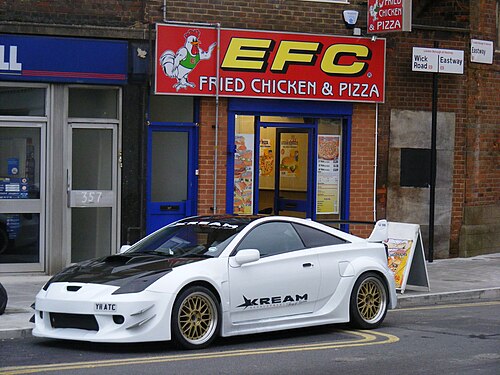 The corner of Wick Road and Eastway, a fried chicken shop in a red brick parade with the borough street signs above it and a modified white Celica on the double yellows.