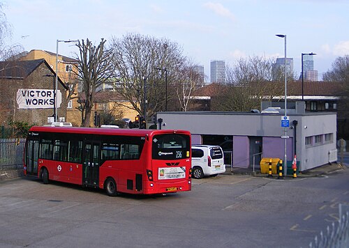 The bus stand on Eastway, a single decker turning round on the yard in front of a low flat roofed office, with a Victory Works sign on the building behind.