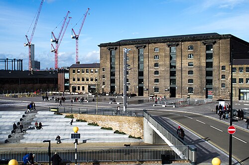 The granary building across Granary Square, six storeys of brick with the canal steps in the foreground and tower cranes working behind it.