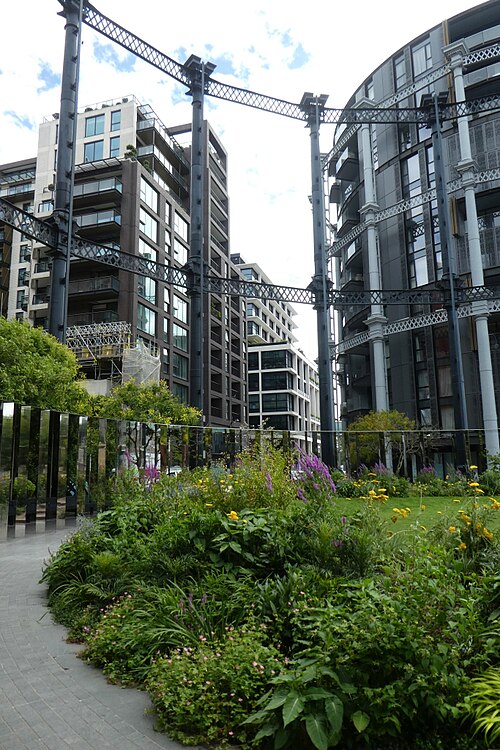 A cast iron gasholder frame standing around a planted garden, with the flats built inside a second frame on the right.